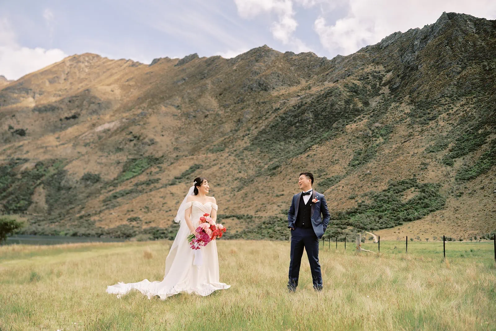 Queenstown Elopement Heli Wedding Photographer クイーンズタウン結婚式 | A bride and groom having a pre-wedding photoshoot in a field with mountains in the background.