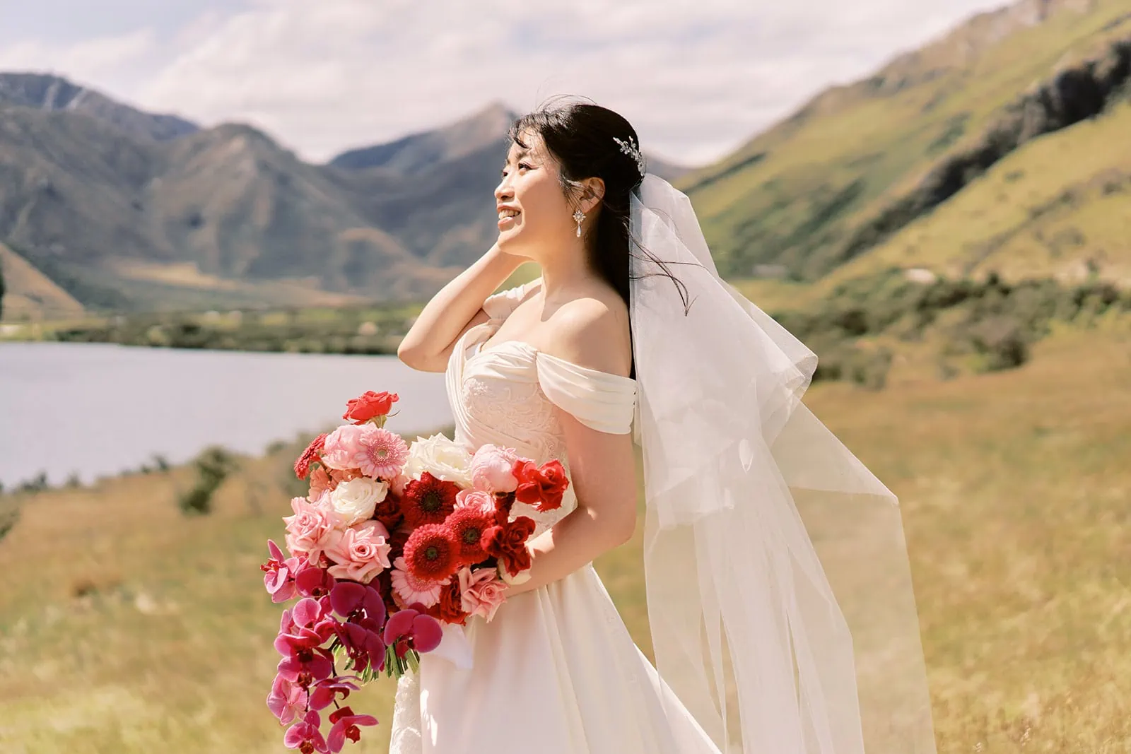 Queenstown Elopement Heli Wedding Photographer クイーンズタウン結婚式 | A bride gracefully poses with her bouquet during a pre-wedding photoshoot in a picturesque field with majestic mountains as the stunning backdrop.
