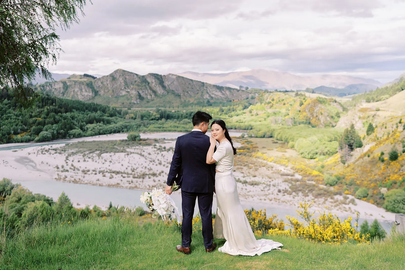 Queenstown Elopement Heli Wedding Photographer クイーンズタウン結婚式 | Pre-wedding photoshoot of a man and woman standing on a hill with mountains and trees.