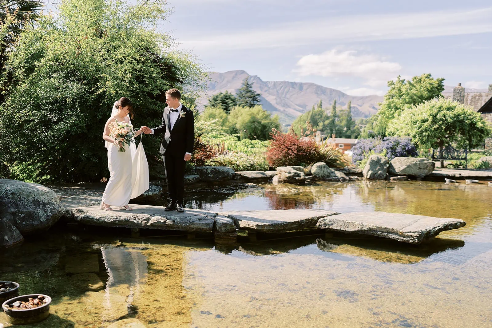 Queenstown Elopement Heli Wedding Photographer クイーンズタウン結婚式 | MJ, the bride, and Shane, the groom, standing in front of a picturesque pond at Stoneridge wedding venue.