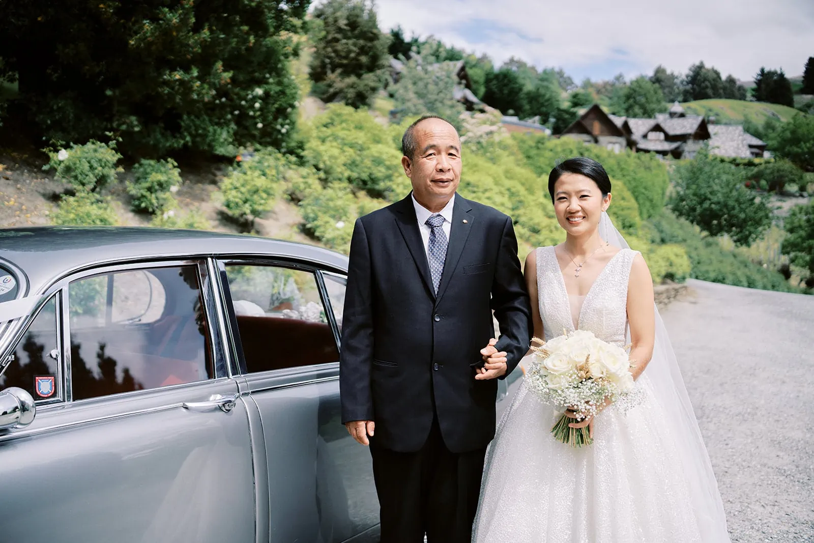 Queenstown Elopement Heli Wedding Photographer クイーンズタウン結婚式 | Joel and Meng, the bride and her father, are seen standing next to a vintage car at Stoneridge Estate.