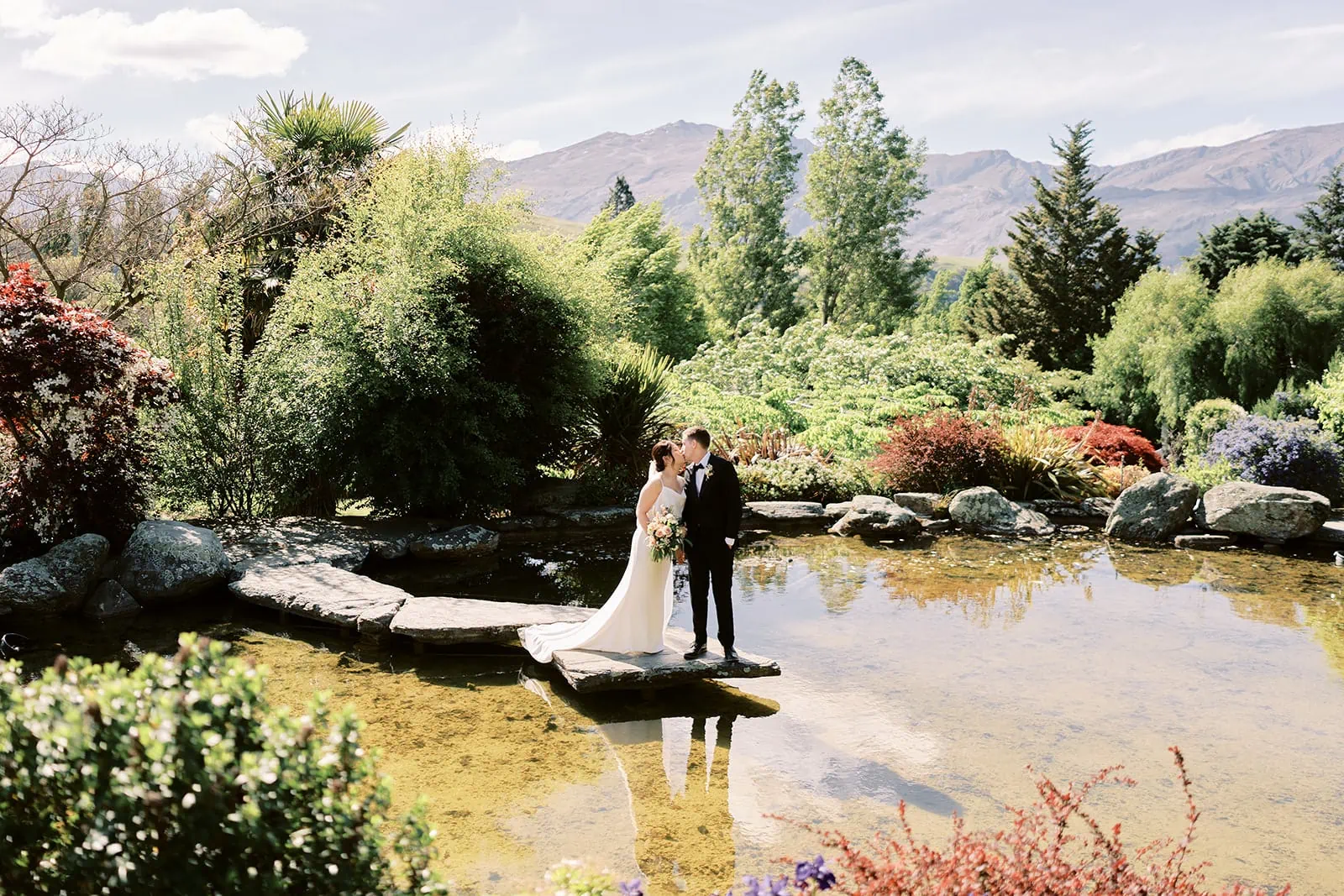 Queenstown Elopement Heli Wedding Photographer クイーンズタウン結婚式 | A Stoneridge Queenstown wedding captures the joyous moments of a bride and groom standing on a bridge in front of a pond.