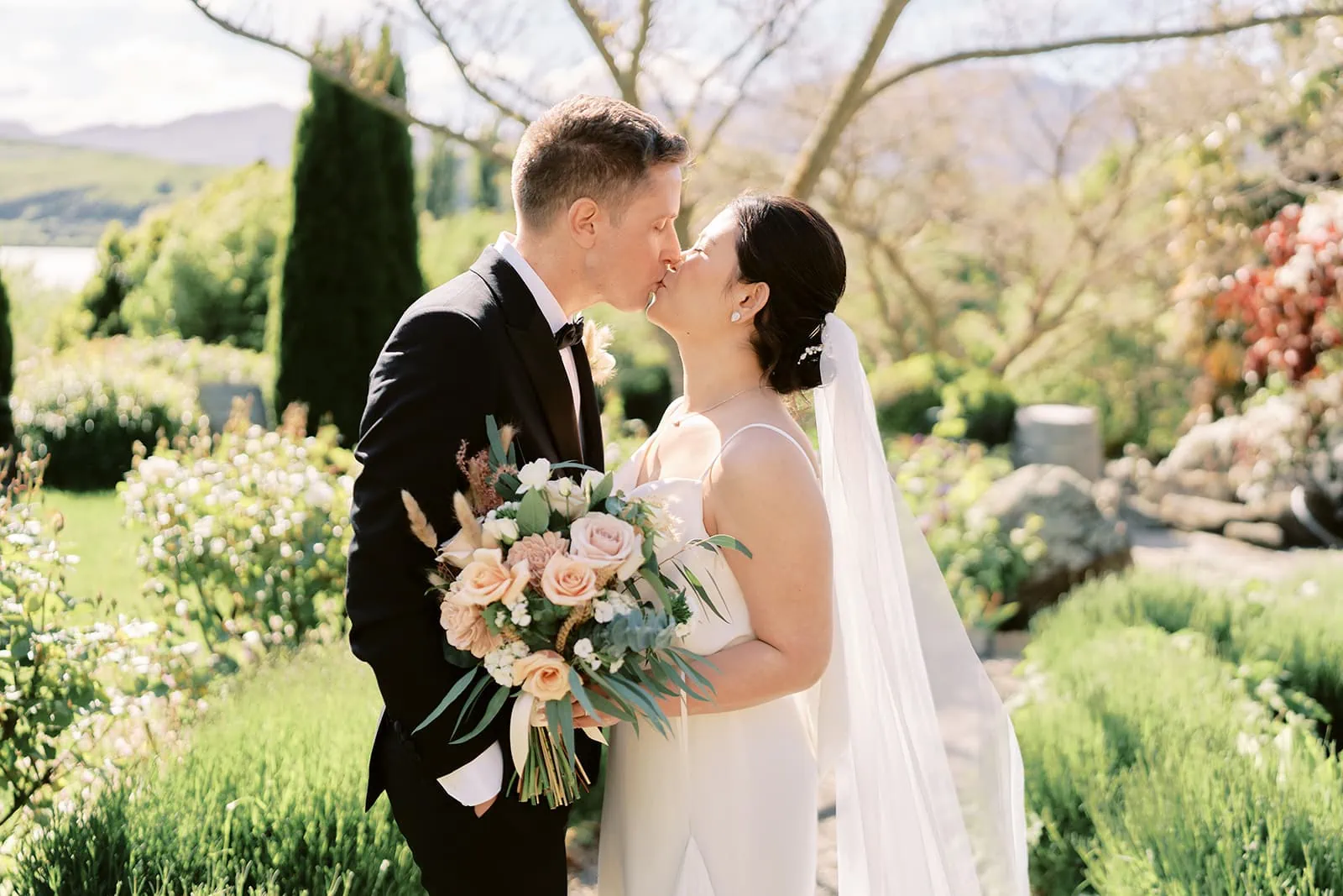 Queenstown Elopement Heli Wedding Photographer クイーンズタウン結婚式 | Mj and Shane, a bride and groom, sharing a romantic kiss during their beautiful garden wedding.