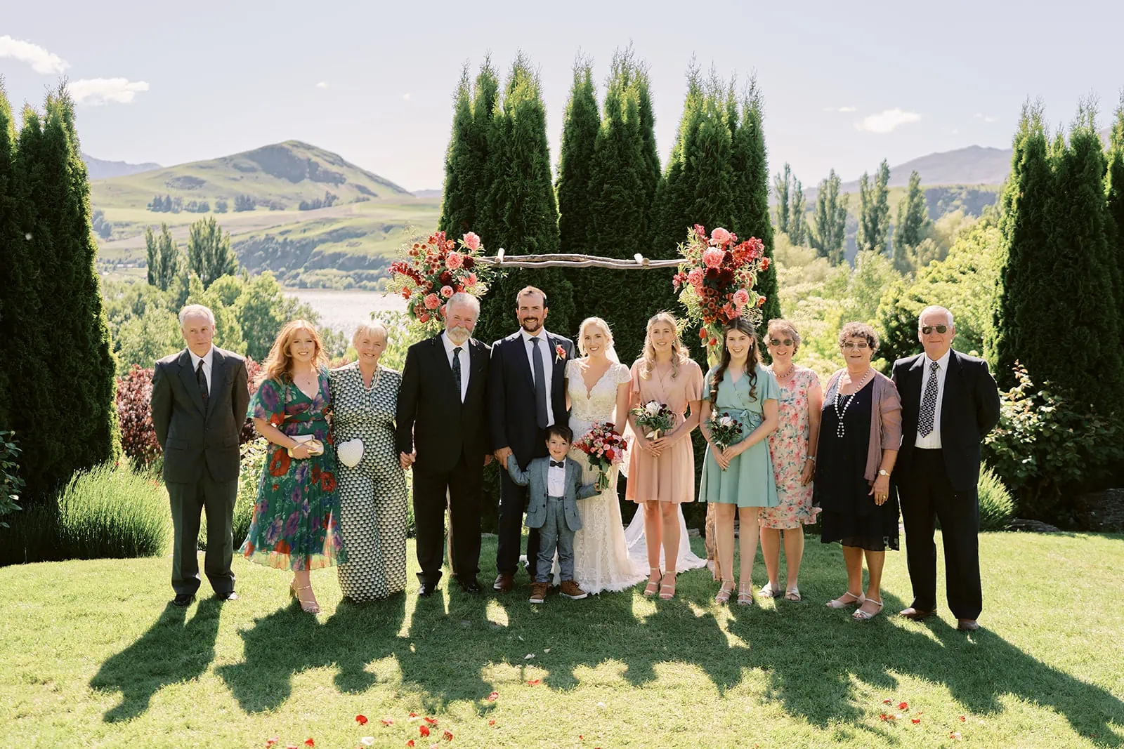 Queenstown Elopement Heli Wedding Photographer クイーンズタウン結婚式 | James and Emily's wedding party posing for a photo in front of Queenstown Stoneridge Estate, with a mountain backdrop.