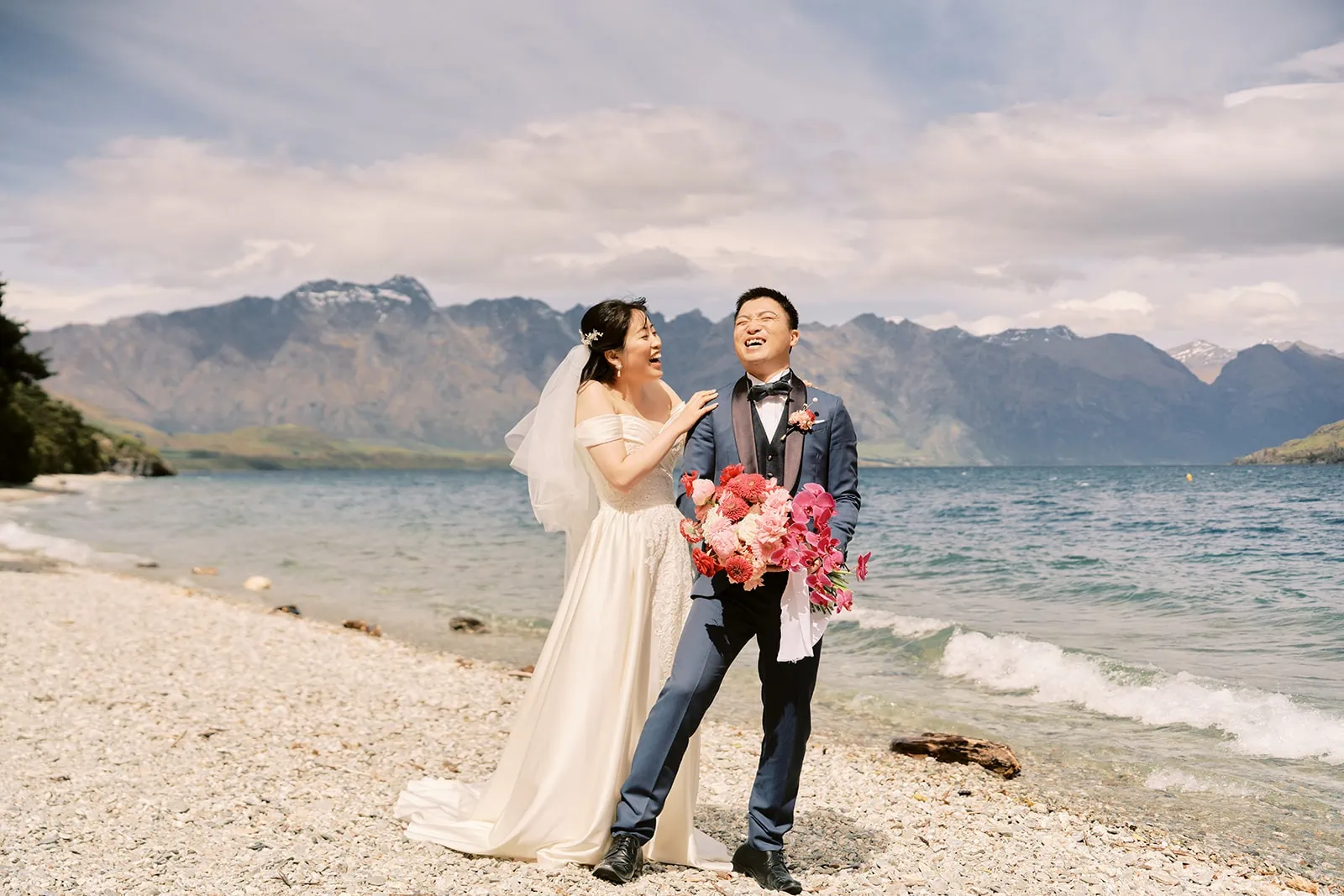 Queenstown Elopement Heli Wedding Photographer クイーンズタウン結婚式 | A pre-wedding photoshoot of a bride and groom on a beach with mountains in the background.