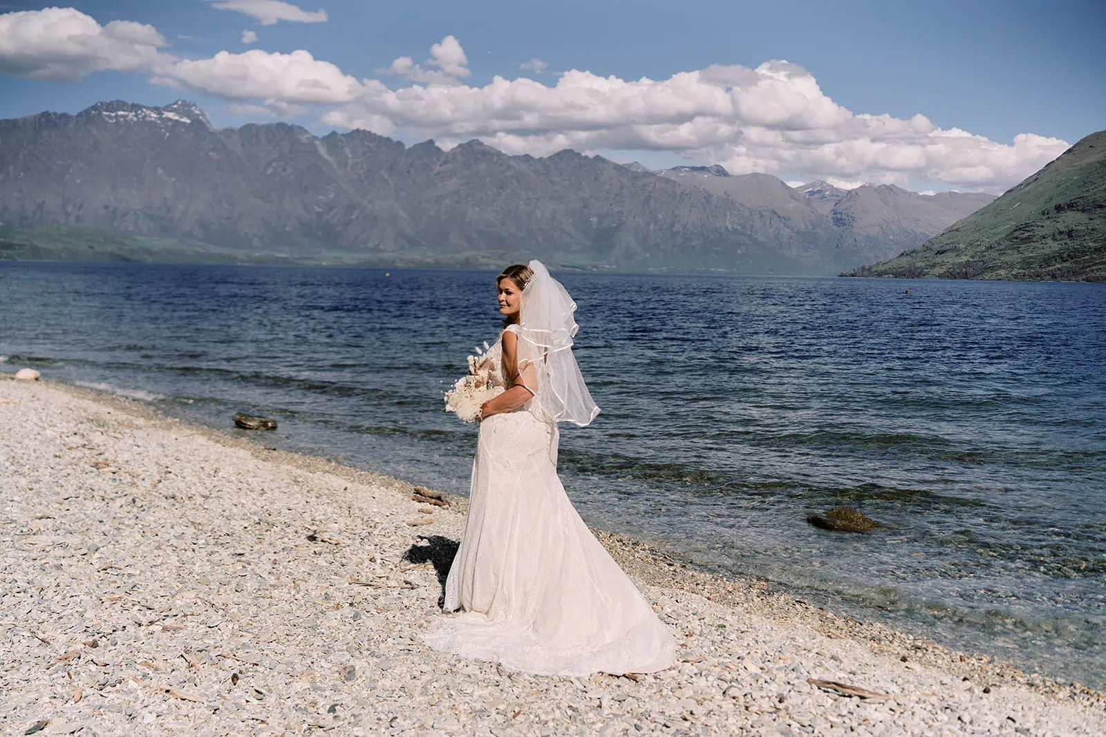 Queenstown Elopement Heli Wedding Photographer クイーンズタウン結婚式 | Melissa, the bride, standing on the shore of Lake Wanaka near Kamana Lakehouse.