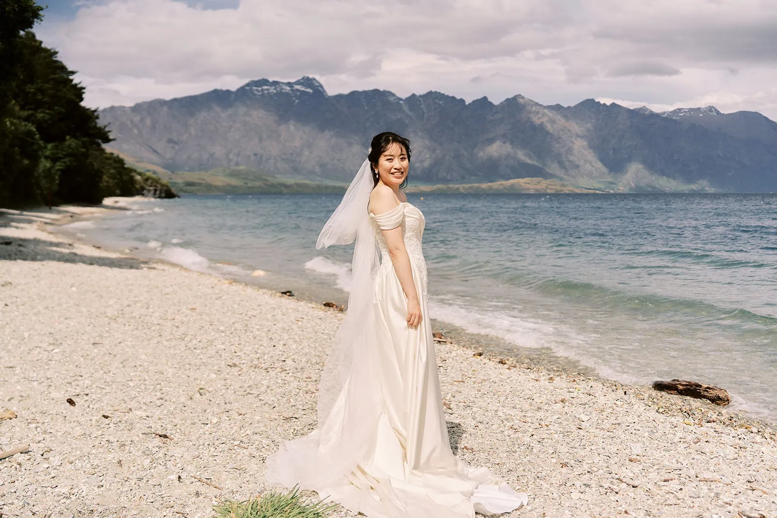 Queenstown Elopement Heli Wedding Photographer クイーンズタウン結婚式 | A bride having a pre-wedding photoshoot on the beach, with mountains in the background.