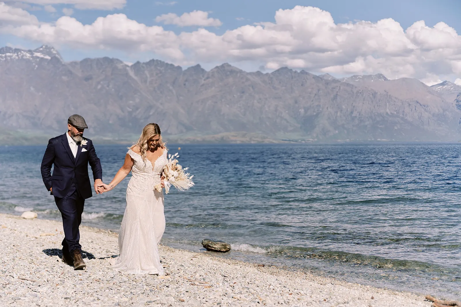 Queenstown Elopement Heli Wedding Photographer クイーンズタウン結婚式 | Melissa and Scott, a bride and groom, walking along the shore of Lake Wanaka.