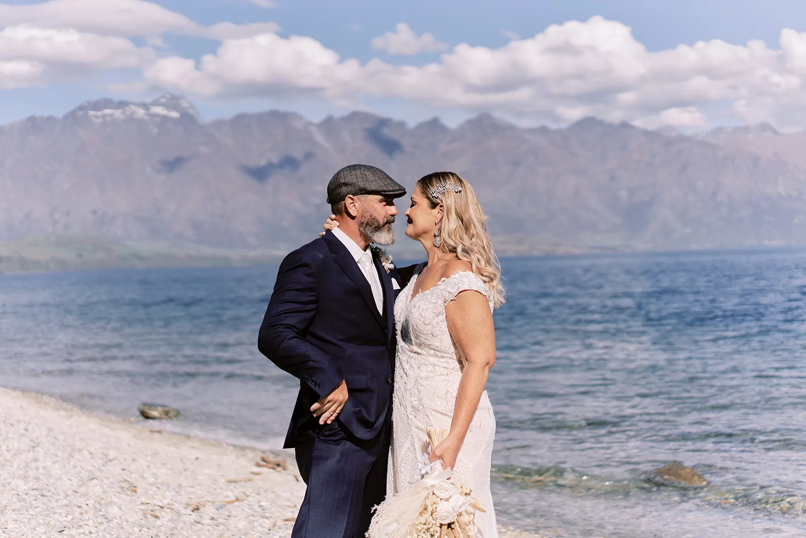 Queenstown Elopement Heli Wedding Photographer クイーンズタウン結婚式 | A bride and groom, Scott and Melissa, standing on the beach of Kamana Lakehouse with mountains in the background.