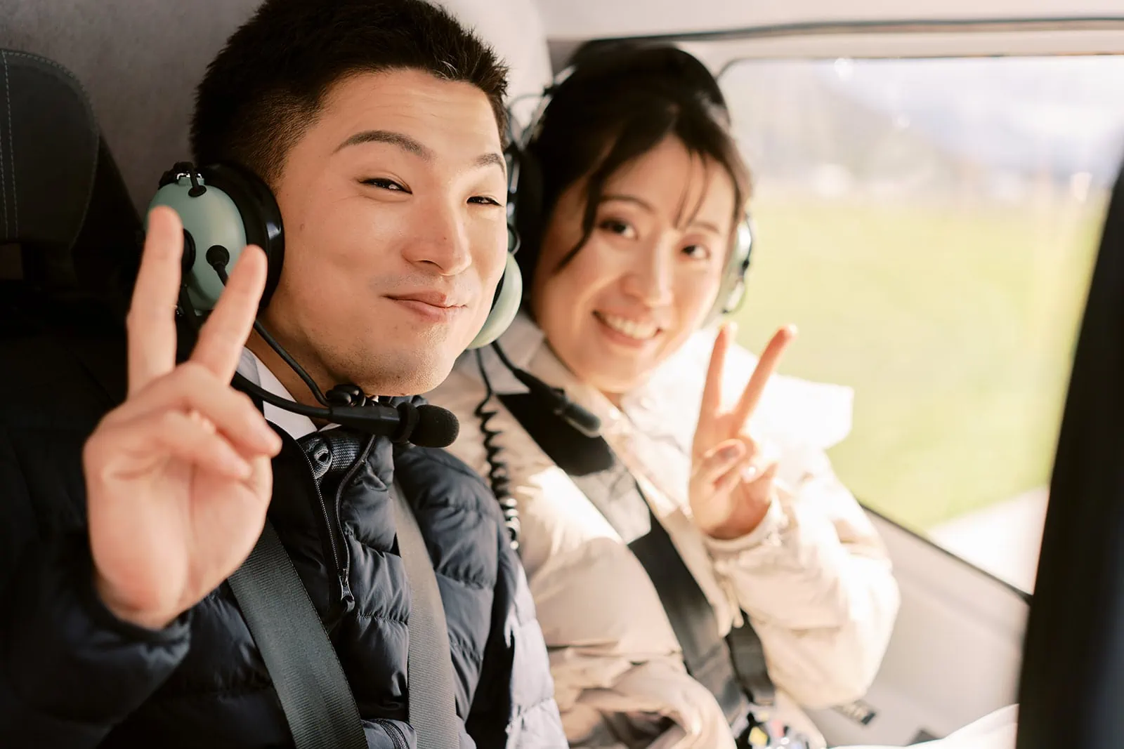 Queenstown Elopement Heli Wedding Photographer クイーンズタウン結婚式 | A man and woman in a helicopter, posing for their pre-wedding photoshoot while giving the peace sign.