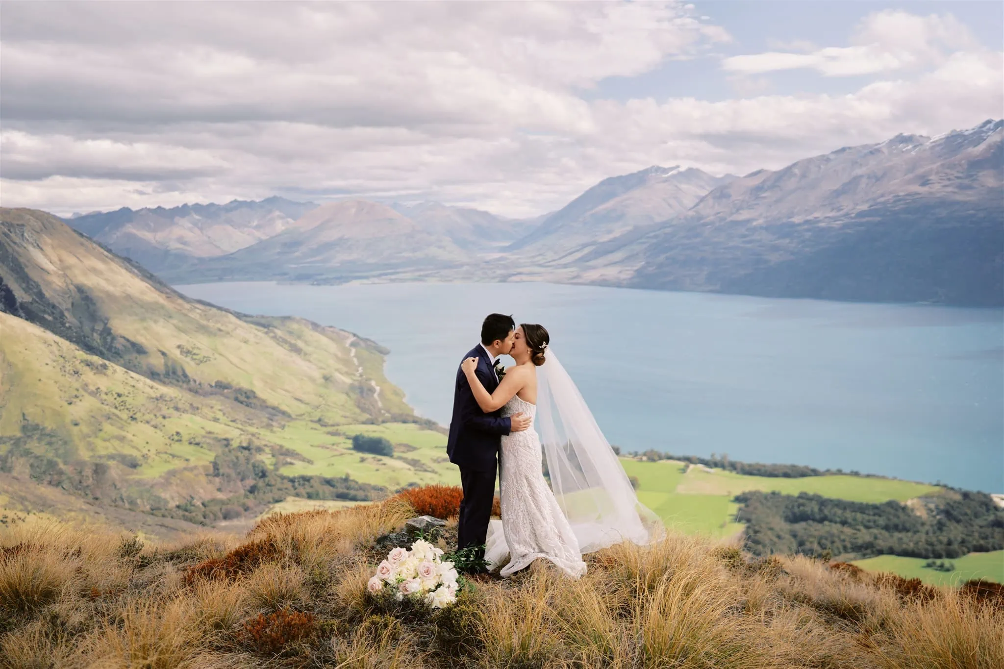 Queenstown Elopement Heli Wedding Photographer クイーンズタウン結婚式 | A bride and groom embarking on an epic journey as they elope, standing on top of a mountain overlooking Lake Wanaka in Queenstown.