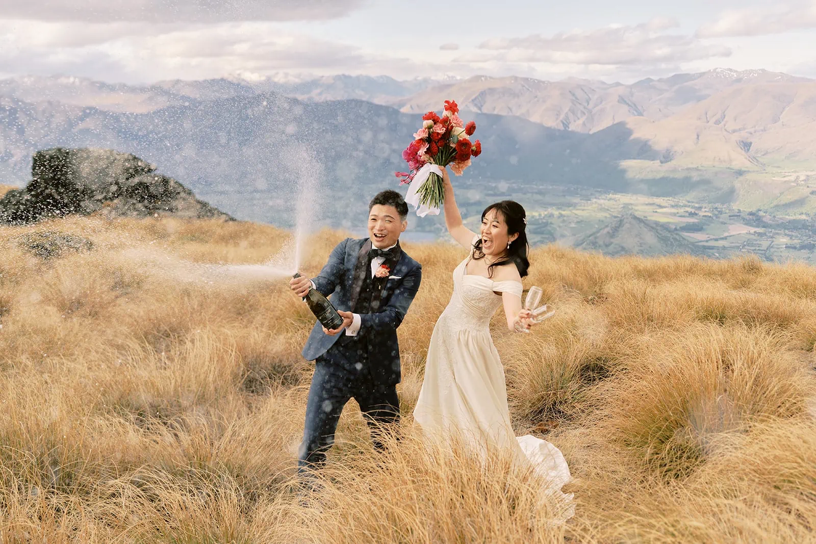 Queenstown Elopement Heli Wedding Photographer クイーンズタウン結婚式 | A bride and groom blowing bubbles during their pre-wedding photoshoot on top of a grassy hill in New Zealand.