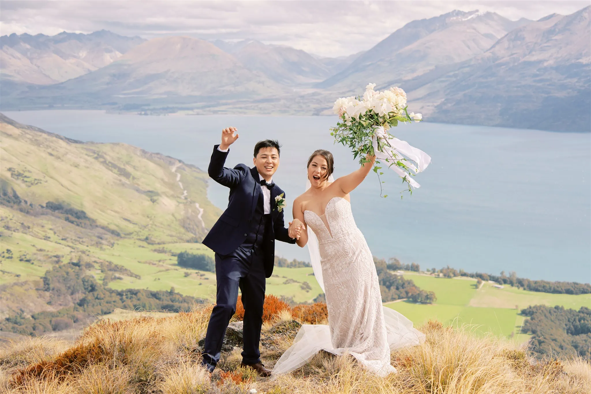 Queenstown Elopement Heli Wedding Photographer クイーンズタウン結婚式 | A bride and groom standing on top of a cliff in Queenstown, New Zealand.