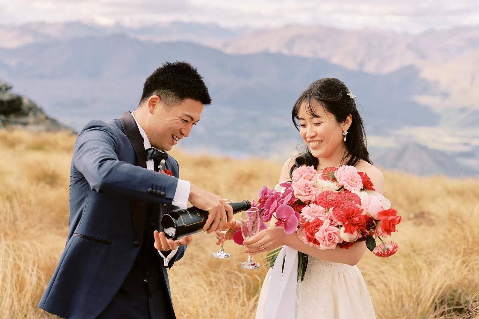 Queenstown Elopement Heli Wedding Photographer クイーンズタウン結婚式 | A pre-wedding photoshoot with a bride and groom pouring wine on top of a hill in New Zealand.