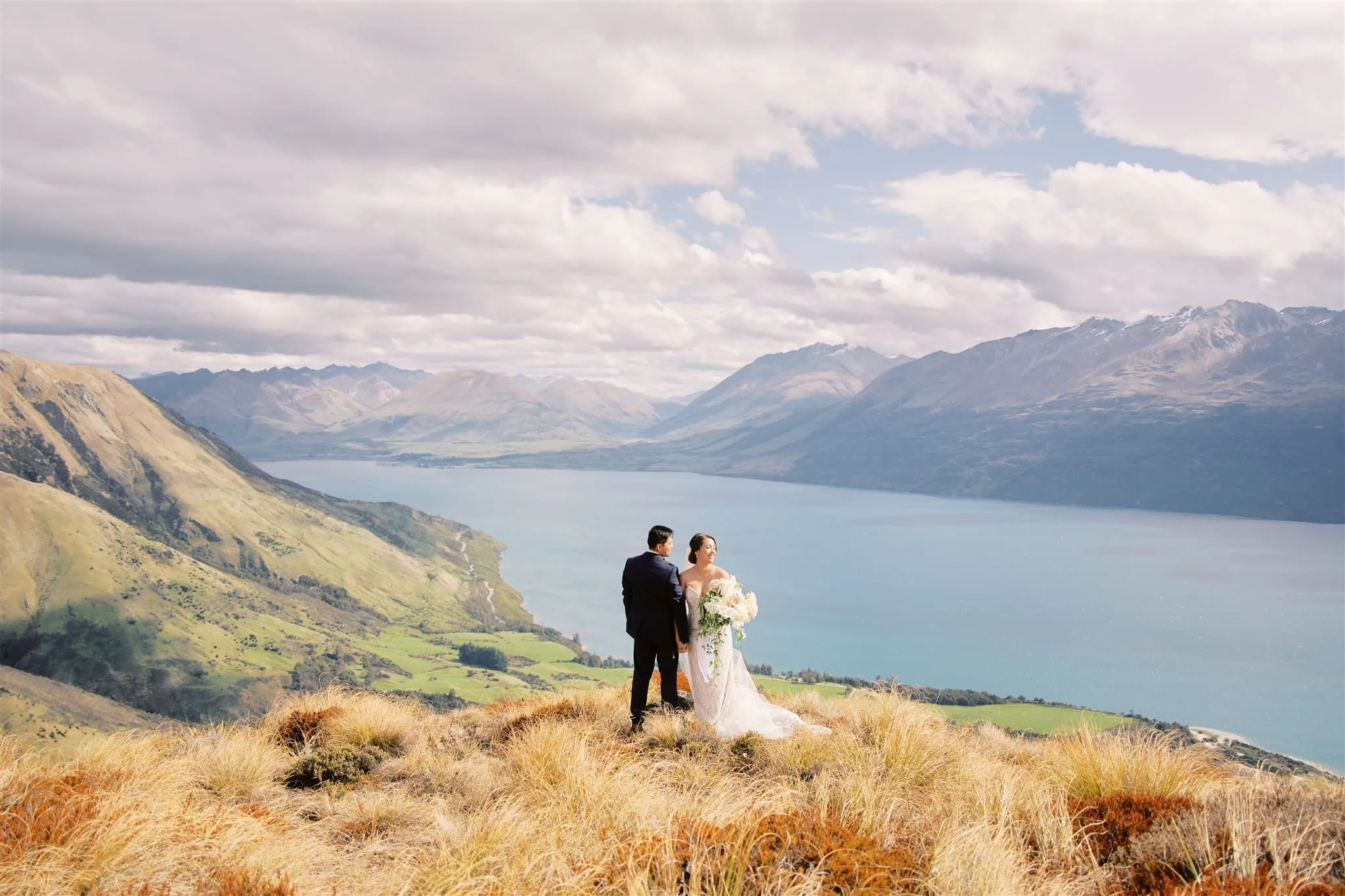 Queenstown Elopement Heli Wedding Photographer クイーンズタウン結婚式 | Mariah and a man standing on a cliff with mountains in the background.