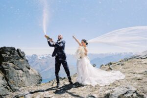 Queenstown Elopement Heli Wedding Photographer クイーンズタウン結婚式 | Gly and Clark, an eloping couple, celebrating their marriage in wedding attire with champagne bottles.