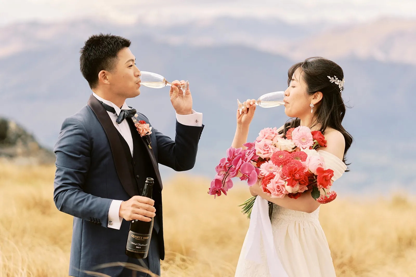 Queenstown Elopement Heli Wedding Photographer クイーンズタウン結婚式 | A couple having a pre-wedding photoshoot in a field in New Zealand, enjoying a glass of wine together.