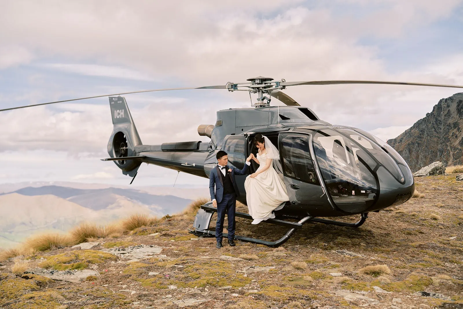 Queenstown Elopement Heli Wedding Photographer クイーンズタウン結婚式 | A bride and groom having their pre-wedding photoshoot next to a helicopter in the mountains.