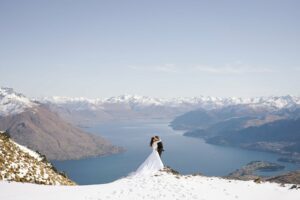 Queenstown Elopement Heli Wedding Photographer クイーンズタウン結婚式 | Kim and Matthew, a bride and groom, standing on top of a snowy mountain overlooking Lake Wanaka during their Queenstown elopement.