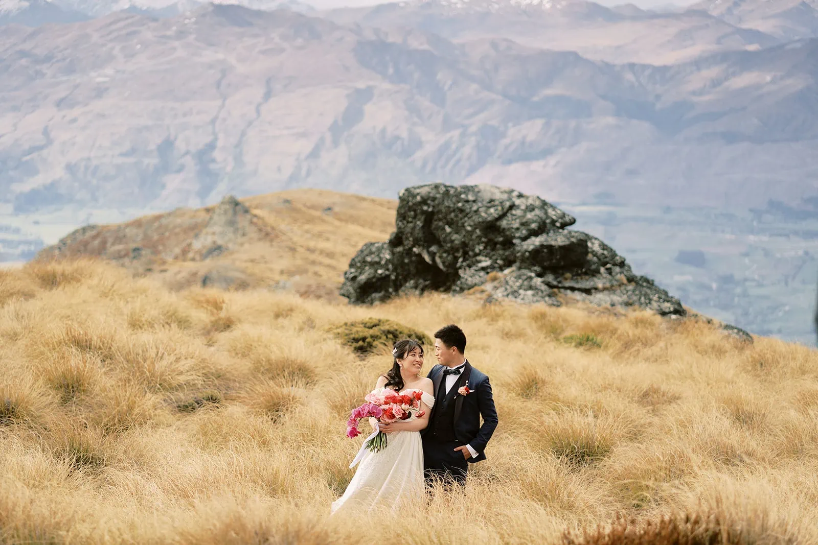 Queenstown Elopement Heli Wedding Photographer クイーンズタウン結婚式 | A bride and groom posing during their pre-wedding photoshoot on a grassy hill in New Zealand.