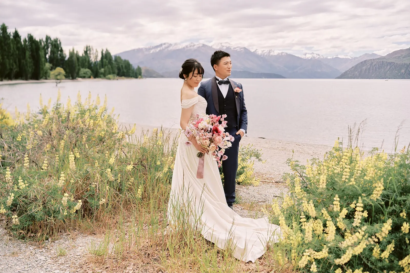 Queenstown Elopement Heli Wedding Photographer クイーンズタウン結婚式 | A pre-wedding photoshoot with a bride and groom standing in front of a lake in New Zealand.