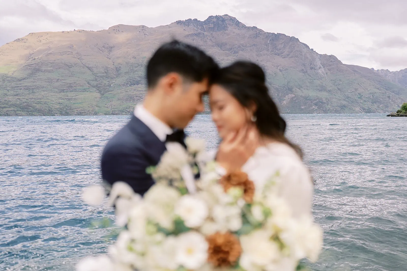Queenstown Elopement Heli Wedding Photographer クイーンズタウン結婚式 | A couple having their pre-wedding photoshoot, standing in front of a picturesque lake with majestic mountains in the background.