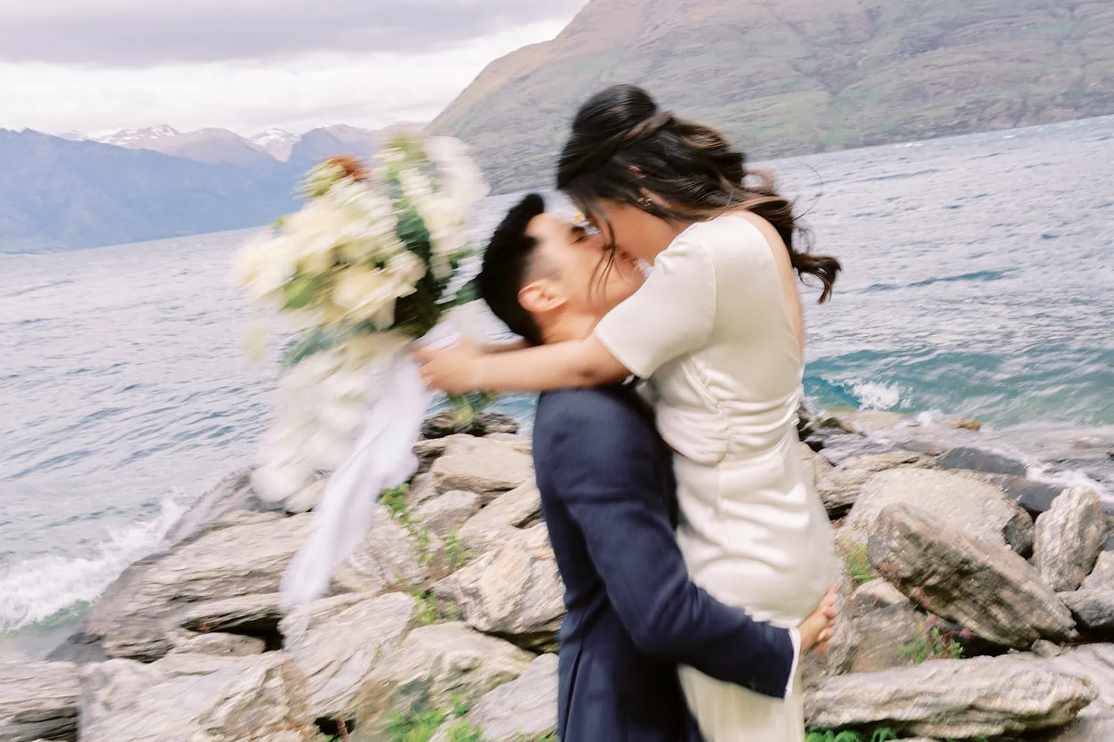 Queenstown Elopement Heli Wedding Photographer クイーンズタウン結婚式 | A pre-wedding photoshoot capturing the intimate moment of a man and woman sharing a passionate kiss on a rocky shore.