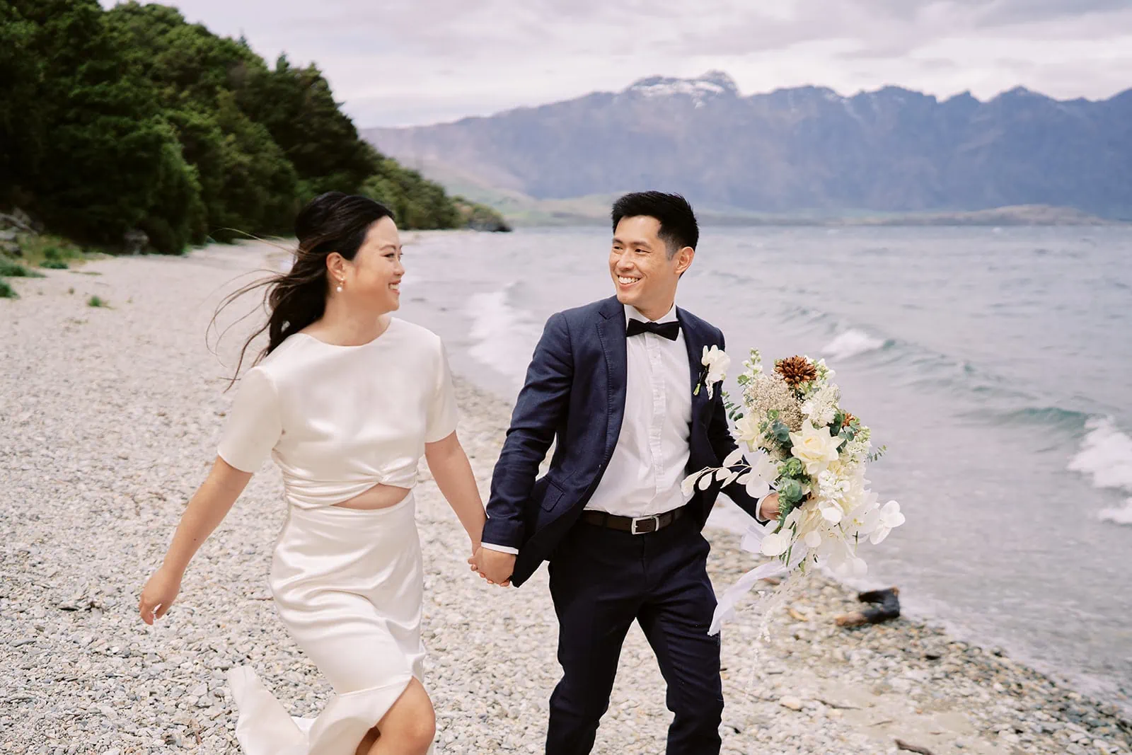 Queenstown Elopement Heli Wedding Photographer クイーンズタウン結婚式 | A couple holding hands and walking on a beach during their pre-wedding photoshoot.