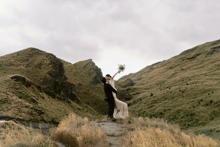 Queenstown New Zealand Heli Wedding Elopement Photographer クイーンズタウン　ニュージーランド　エロープメント 結婚式 | A man and woman kissing in a field during their Queenstown pre-wedding ground level shoot.
