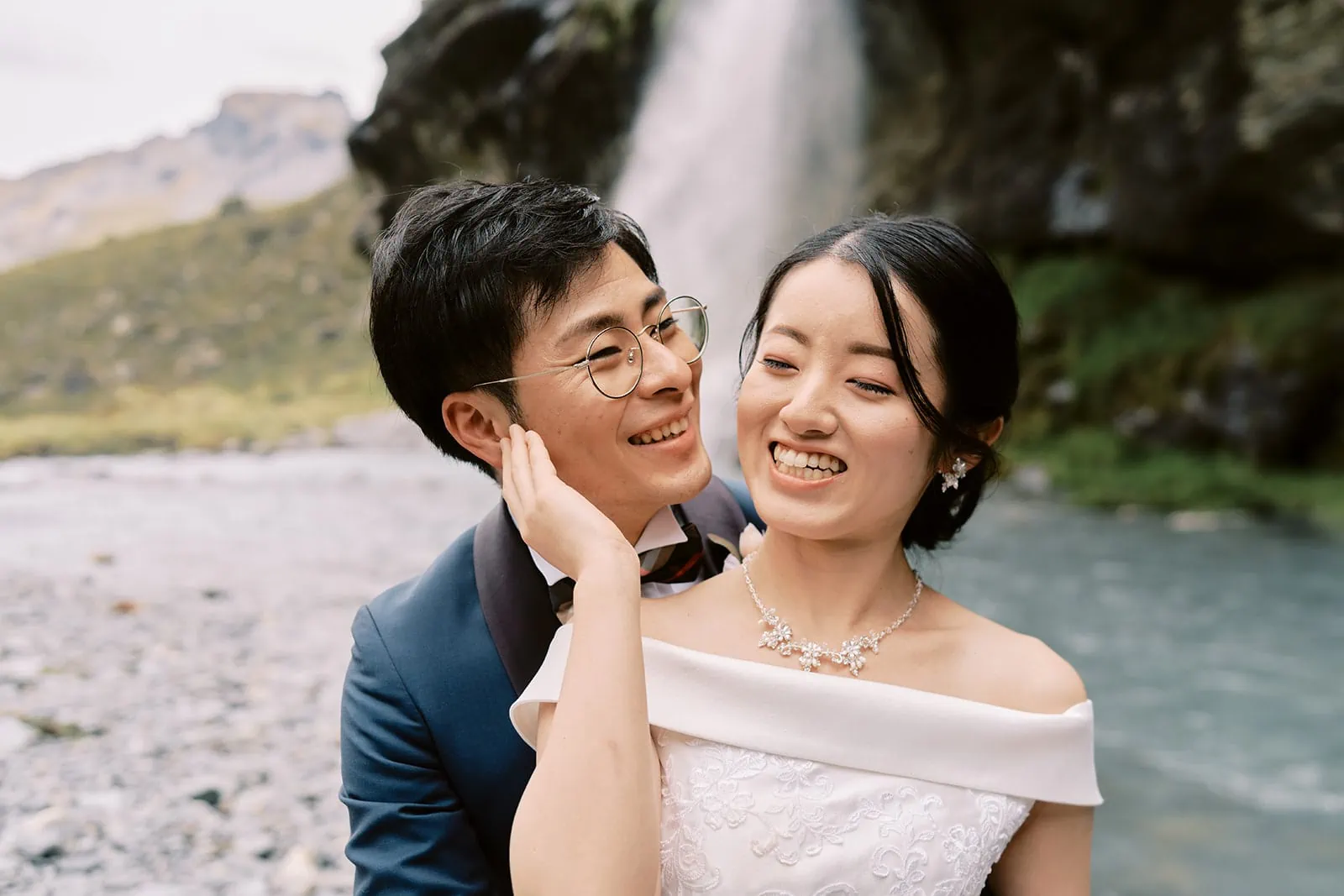 Queenstown Elopement Heli Wedding Photographer クイーンズタウン結婚式 | A bride and groom posing in front of a waterfall during their Queenstown Heli Elopement.