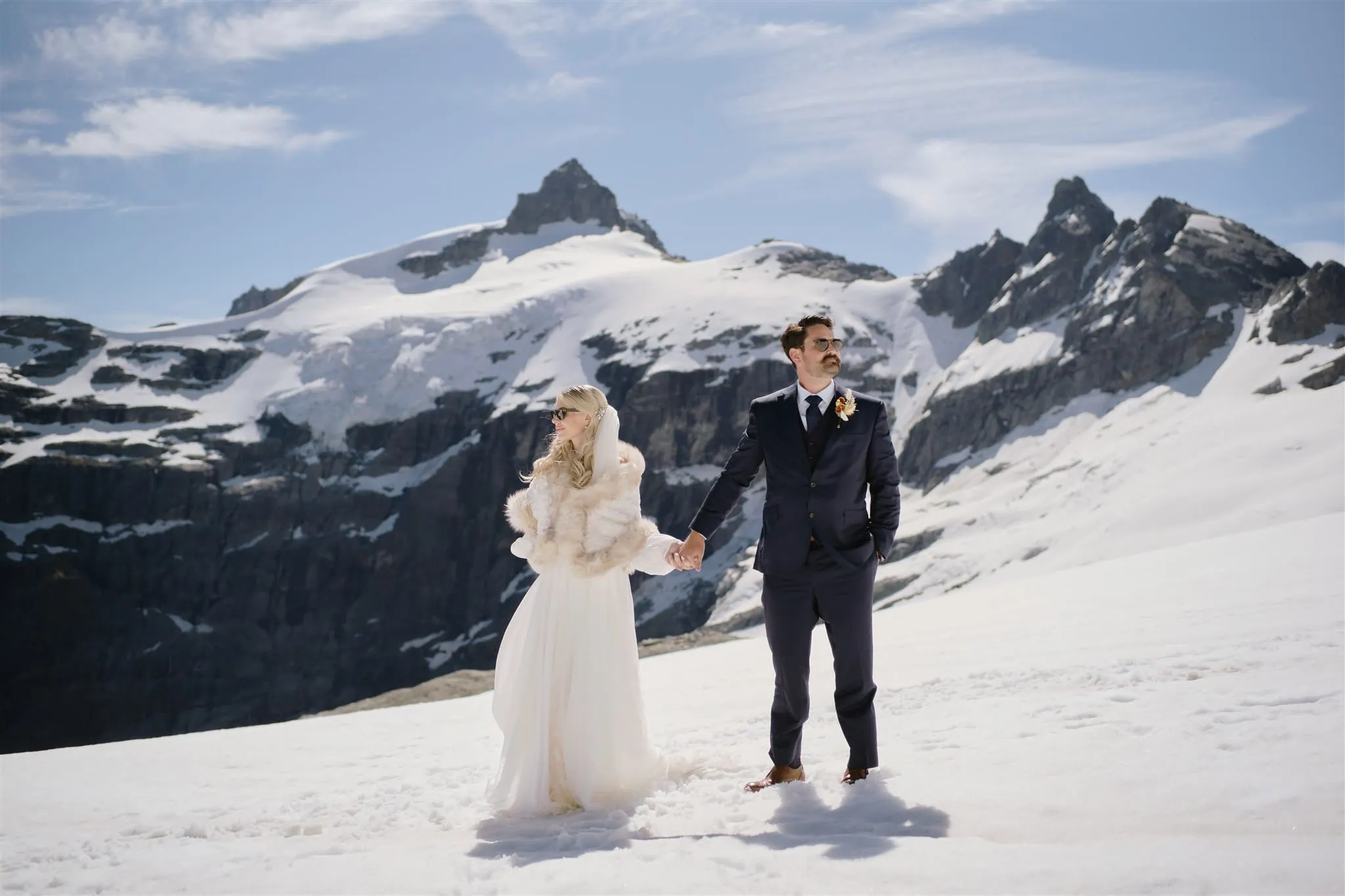 Queenstown New Zealand Heli Wedding Elopement Photographer クイーンズタウン　ニュージーランド　エロープメント 結婚式 | A bride and groom holding hands on a snow-covered mountain landscape during their elopement wedding.