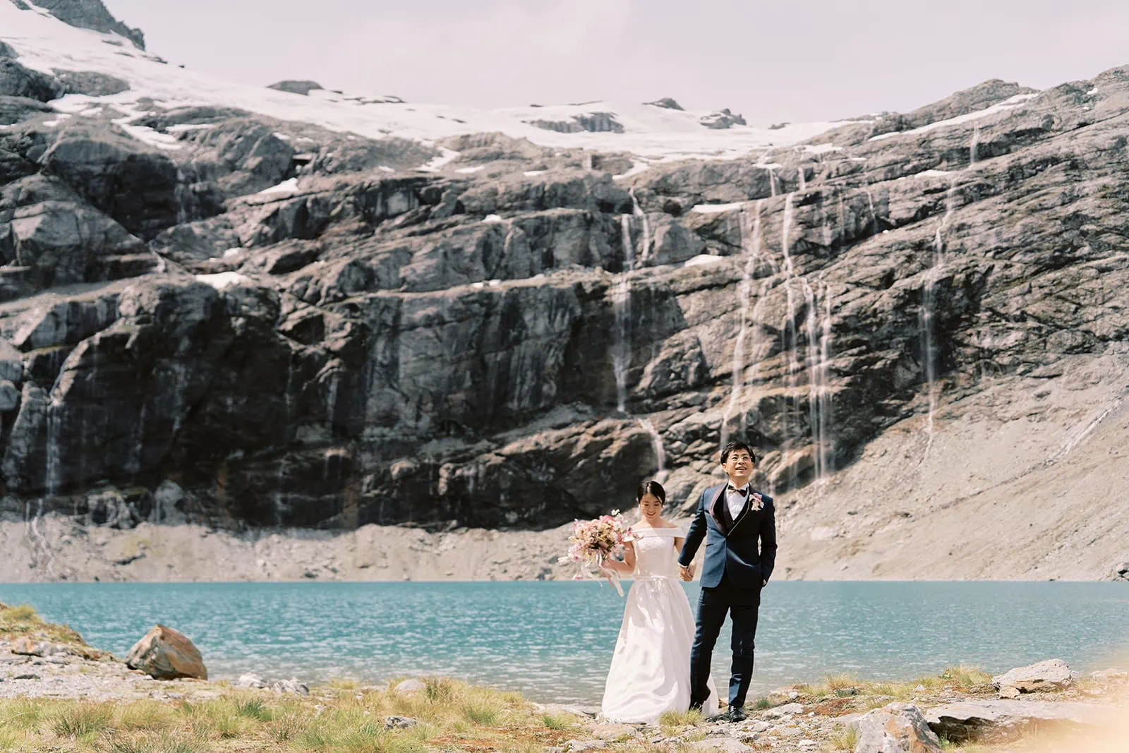 Queenstown Elopement Heli Wedding Photographer クイーンズタウン結婚式 | A bride and groom standing in front of a mountain lake during their Queenstown Heli Elopement.