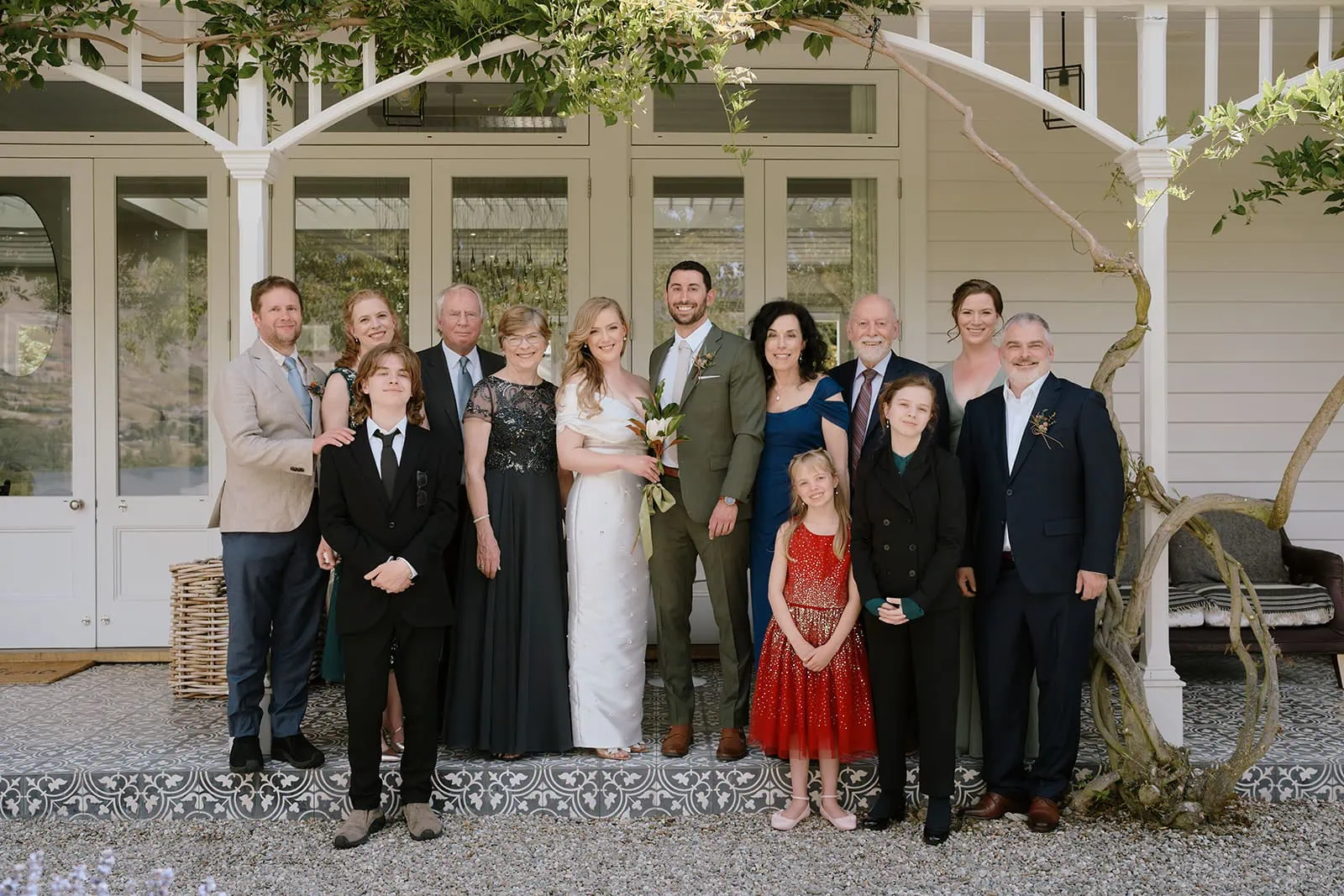 クイーンズタウン　テカポ　ニュージーランド　エロープメント 前撮り　フォトウェディング　結婚式 | クイーンズタウンの結婚式で、庭のある白い家の前で家族写真を撮っている12人のグループ。