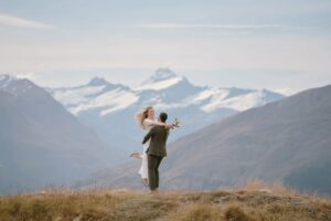 クイーンズタウン　テカポ　ニュージーランド　エロープメント 前撮り　フォトウェディング　結婚式 | クイーンズタウンでの結婚式の際、雪をかぶった山々の頂上を背景に草原で喜びの抱擁を交わすカップル。