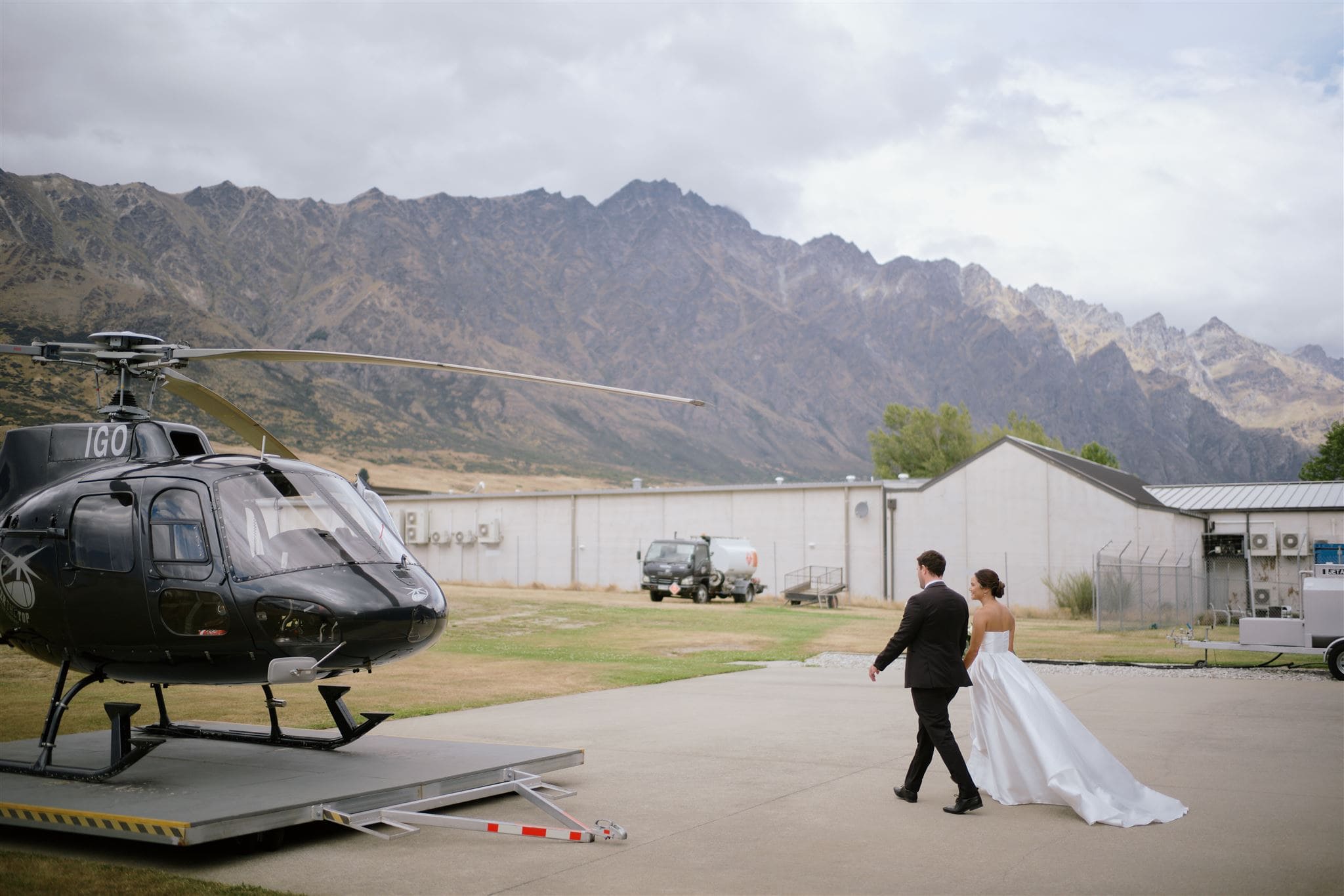 クイーンズタウン　テカポ　ニュージーランド　エロープメント 前撮り　フォトウェディング　結婚式 | クイーンズタウンで、新婚カップルがヘリコプターに向かって歩いている。背景には山々の風景が広がり、結婚式後の出発を暗示している。