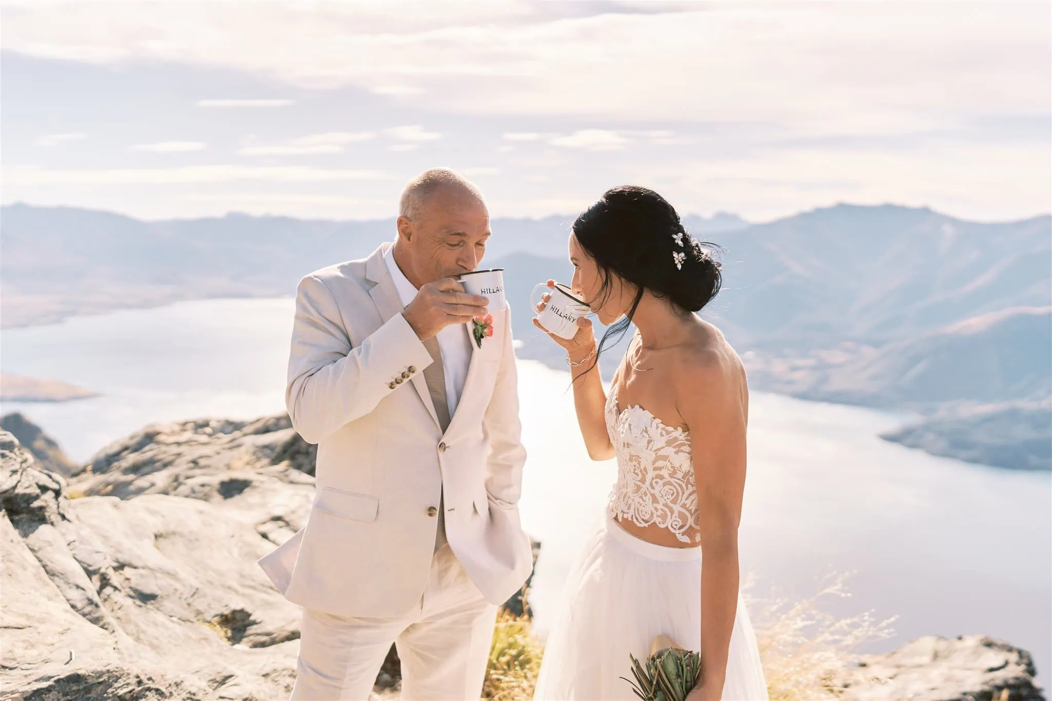 queenstown new zealand heli wedding elopement photographer videographer | A bride and groom sipping tea on a mountain overlook with a lake in the background during their Queenstown elopement.