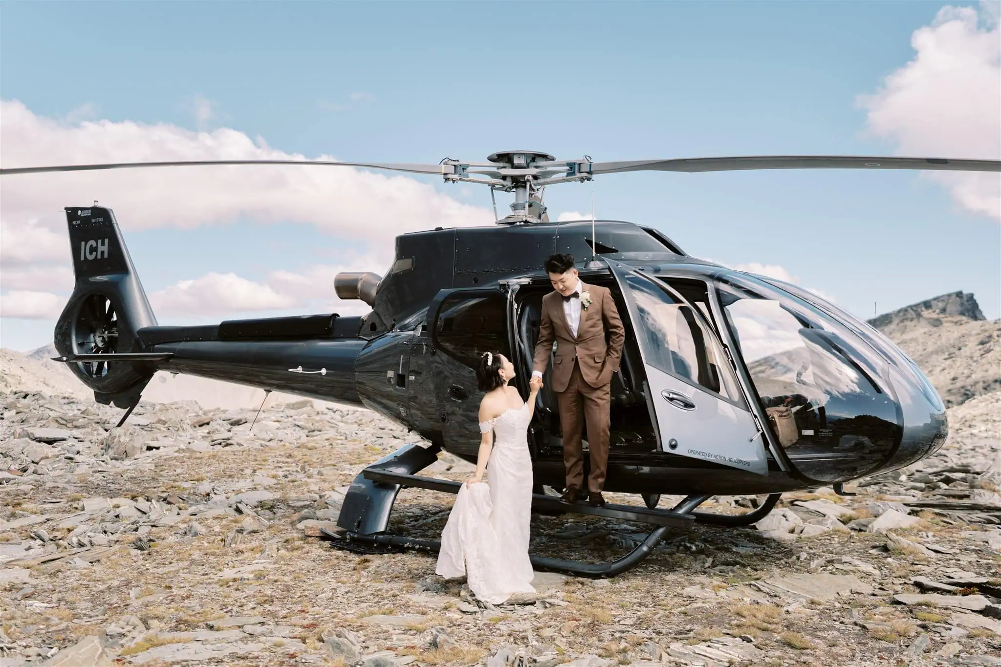 queenstown new zealand heli wedding elopement photographer videographer | A bride and groom by a black helicopter on a rocky mountain, sharing an intimate moment during their Queenstown Heli Elopement.