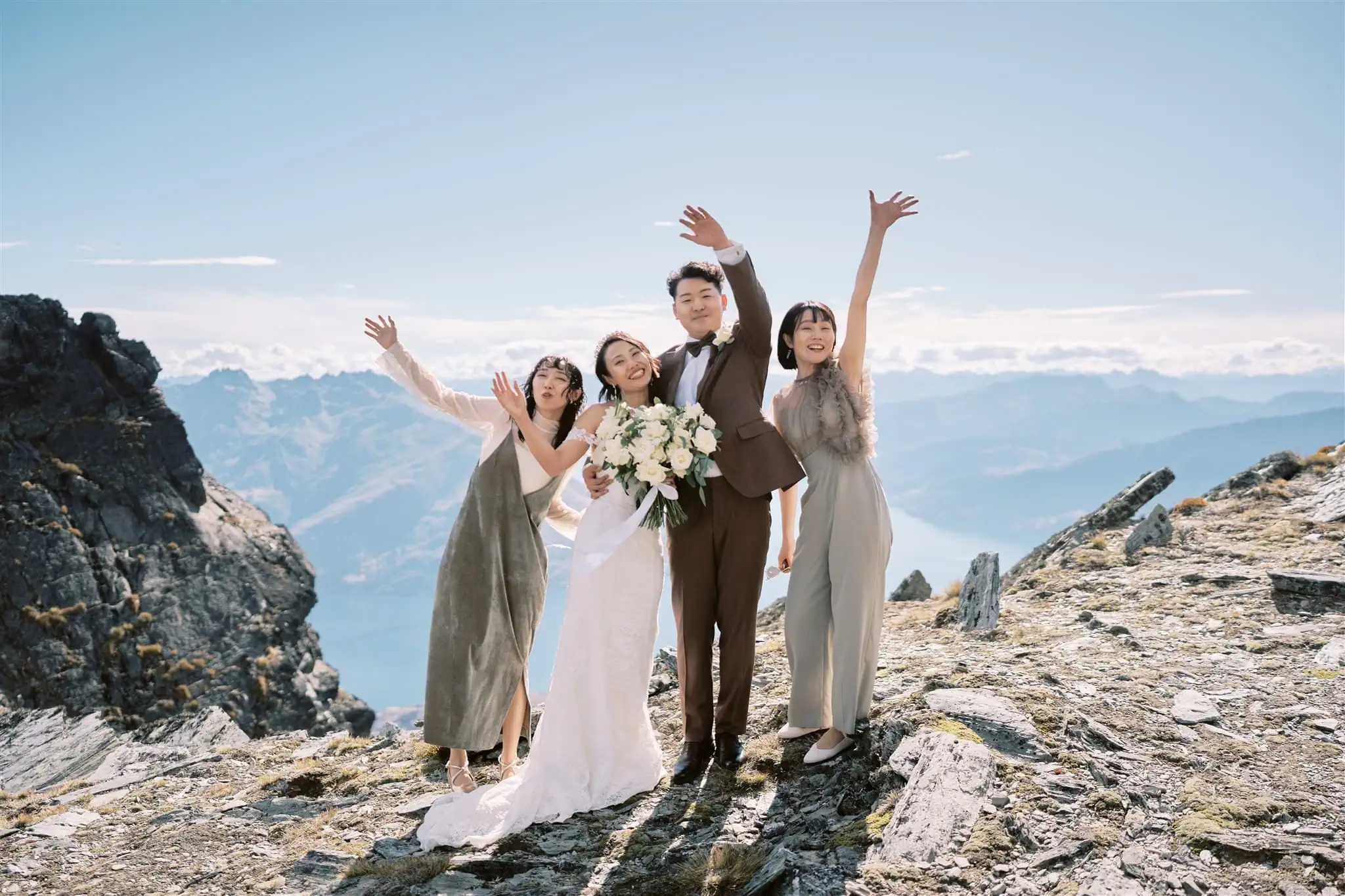 queenstown new zealand heli wedding elopement photographer videographer | Azusa & Yuhei, a wedding couple and two guests, joyfully raising their arms on a mountain summit overlooking a scenic valley during their Queenstown Heli Elopement.