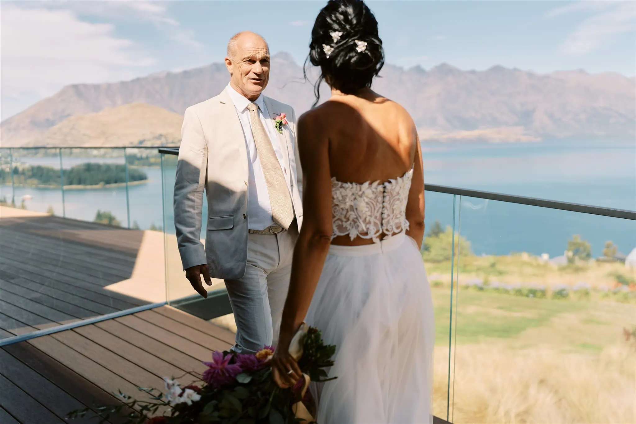 queenstown new zealand heli wedding elopement photographer videographer | Ian and Vivienne stand on a terrace overlooking a lake and mountains in Queenstown, facing each other, with Ian looking at Vivienne.