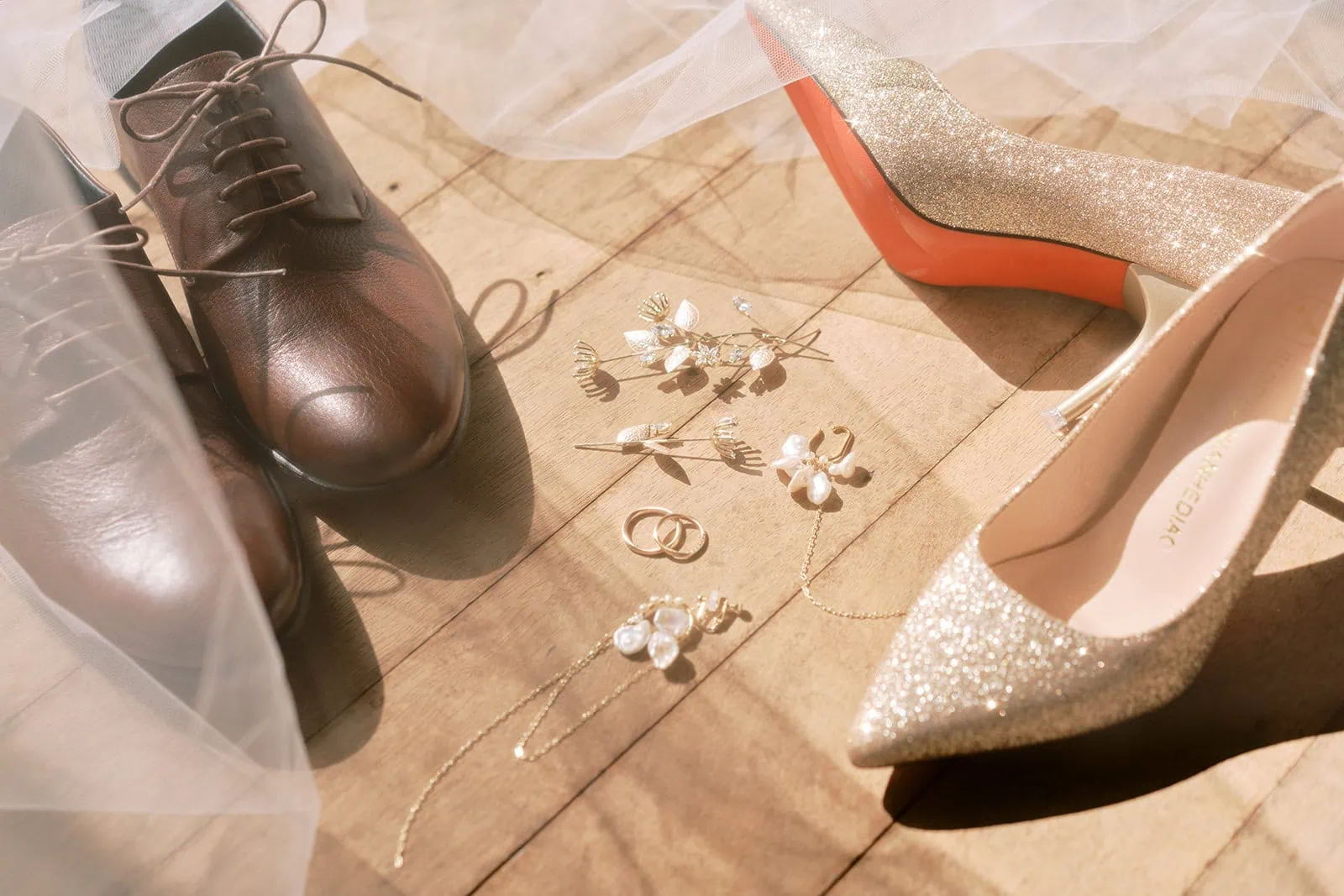 queenstown new zealand heli wedding elopement photographer videographer | A pair of men's brown oxfords, women's glittery high heels, and scattered wedding accessories on a wooden floor captured during a Queenstown pre-wedding shoot.
