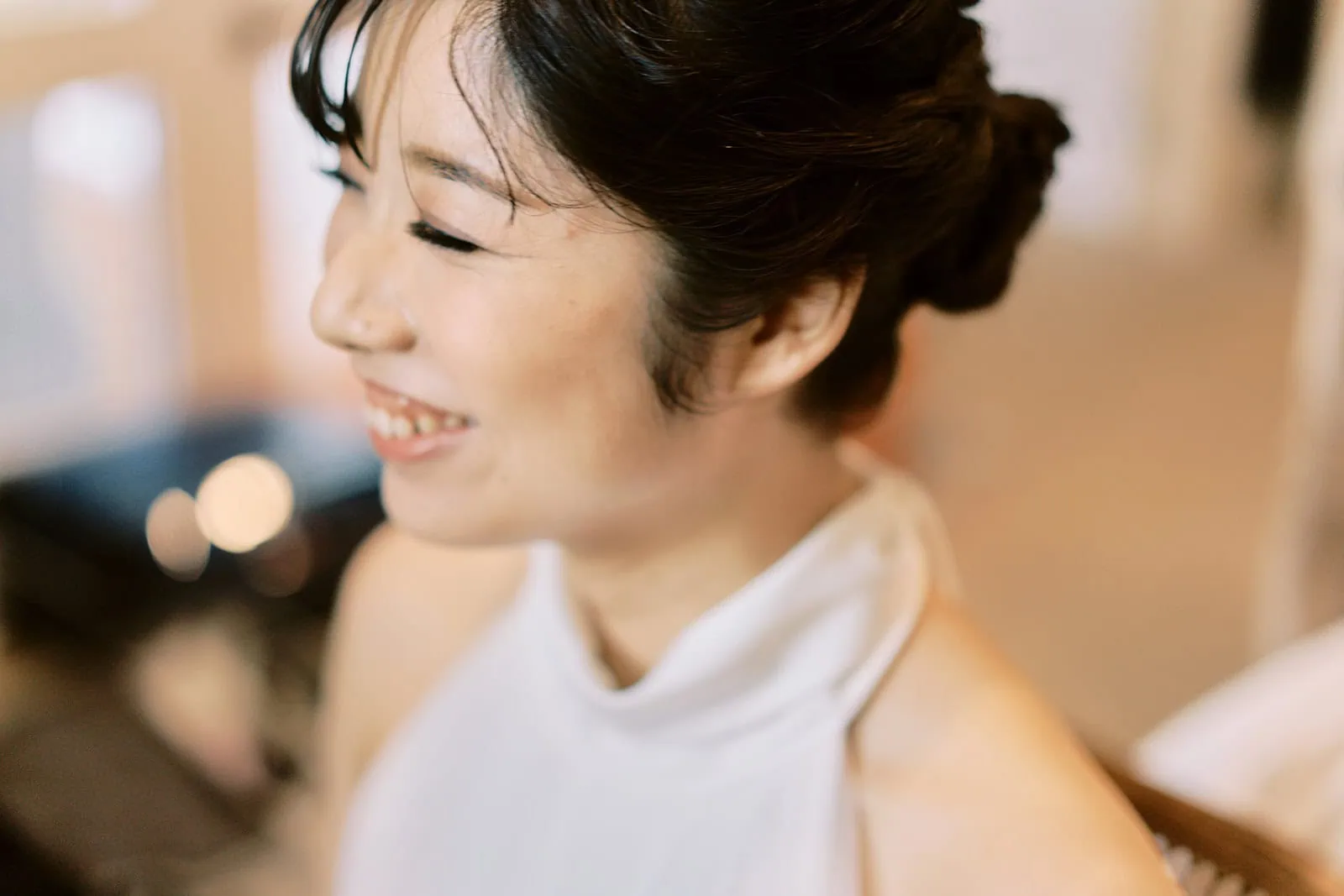 queenstown new zealand heli wedding elopement photographer videographer | A smiling Asian woman with an elegant updo hairstyle, wearing a white dress in a softly lit room during her Queenstown pre-wedding shoot.