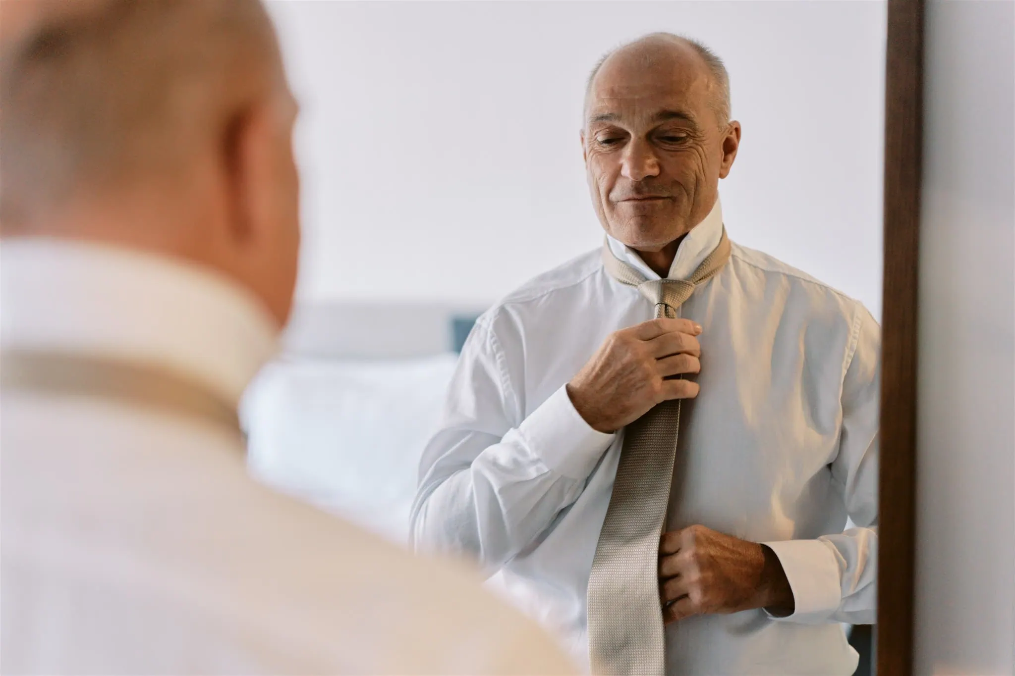 queenstown new zealand heli wedding elopement photographer videographer | A mature man adjusting his tie while looking at his reflection in a mirror, preparing for his Queenstown elopement.