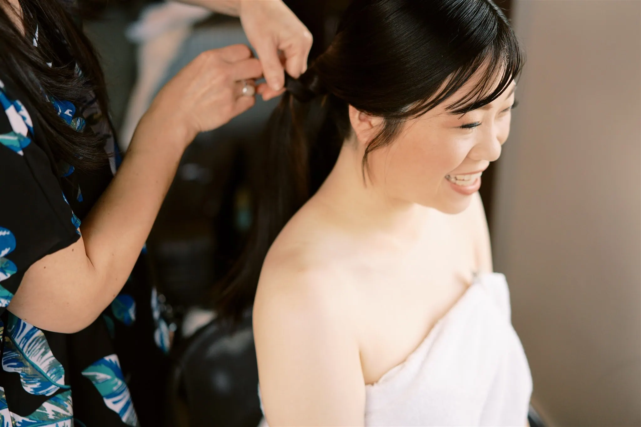 queenstown new zealand heli wedding elopement photographer videographer | A woman is having her hair styled by another person. She is smiling and wearing a white towel, perfectly capturing the excitement of a special day, as seen through the lens of a Queenstown wedding photographer.