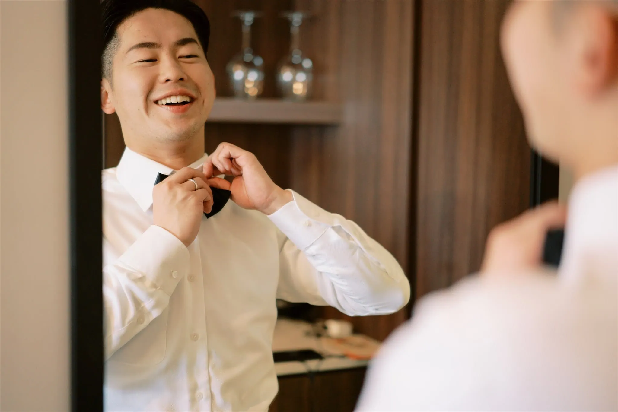 queenstown new zealand heli wedding elopement photographer videographer | A man smiles while adjusting his bow tie in front of a mirror, captured perfectly by a Queenstown wedding photographer.