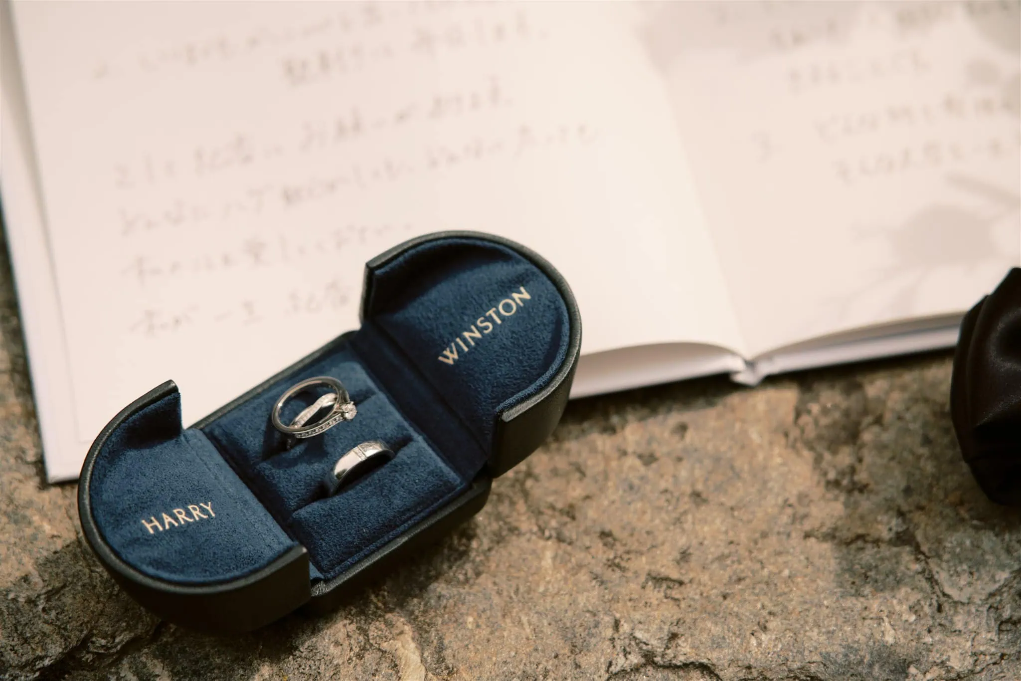 queenstown new zealand heli wedding elopement photographer videographer | A Harry Winston ring box containing two rings sits on a stone surface, with an open book featuring handwritten notes in the background, as captured by a skilled Queenstown wedding photographer.