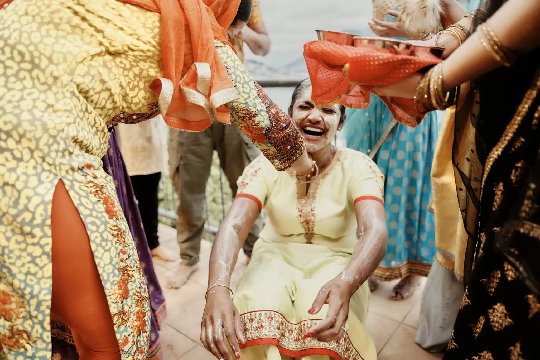 queenstown new zealand heli wedding elopement photographer videographer | A joyful woman in traditional attire is being smeared with white paste during a celebratory outdoor event. Others in colorful clothing surround her with smiles and laughter, reminiscent of a Queenstown elopement's vibrant spirit captured through exquisite wedding photography.