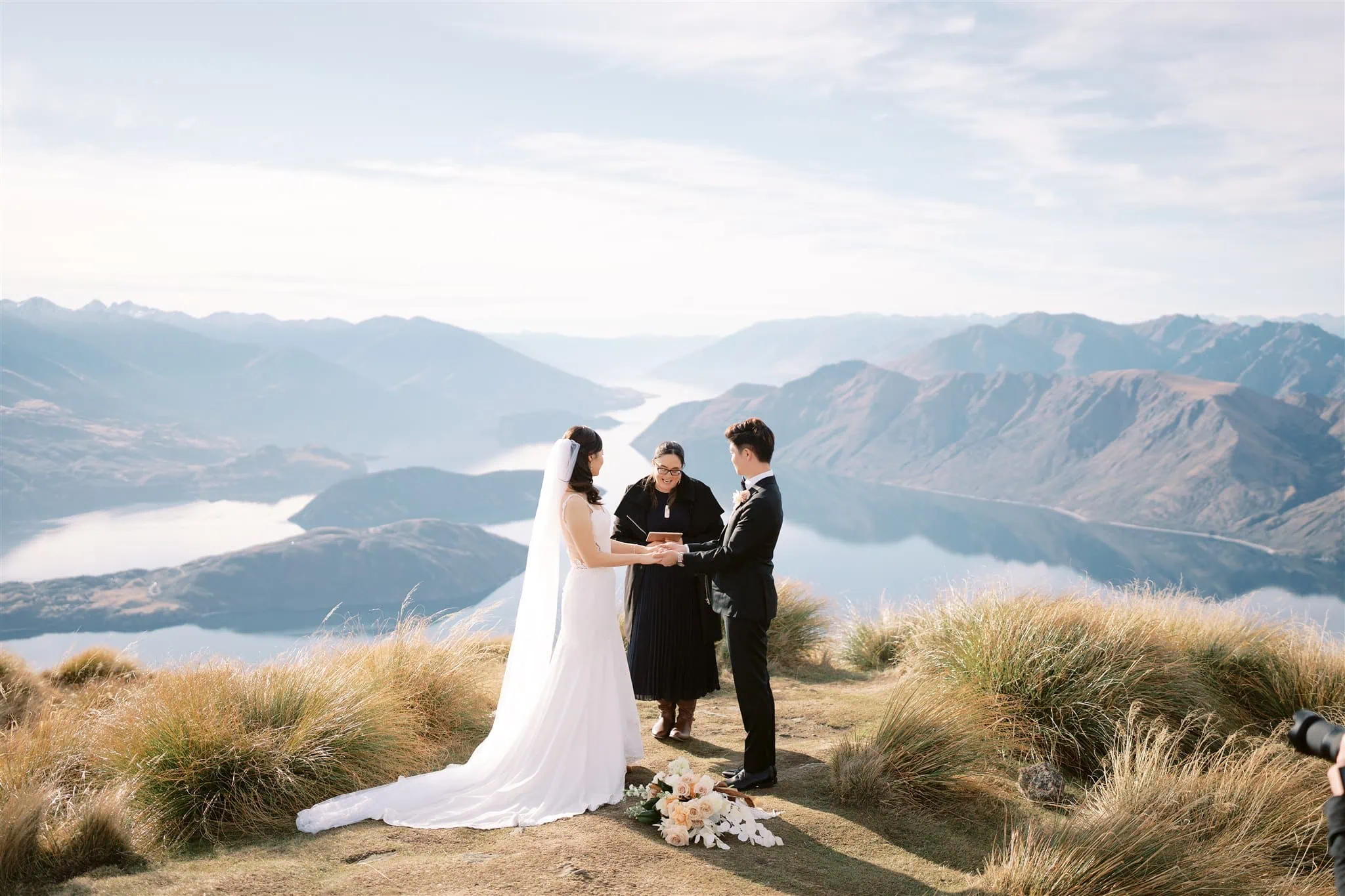 queenstown new zealand heli wedding elopement photographer videographer | A couple elopes to a grassy hilltop in Queenstown, exchanging vows amidst breathtaking lakes and mountains, all captured through stunning wedding photography.