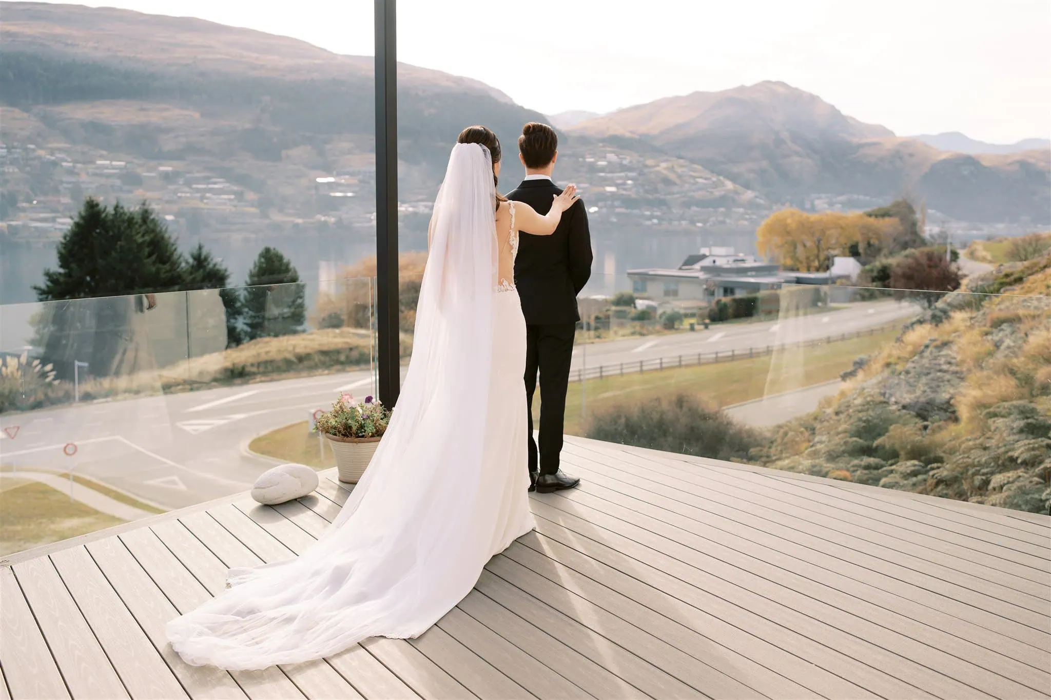 queenstown new zealand heli wedding elopement photographer videographer | A bride and groom stand on a deck overlooking the breathtaking Queenstown landscape, with mountains and a shimmering lake—a perfect moment captured by skillful wedding photography.