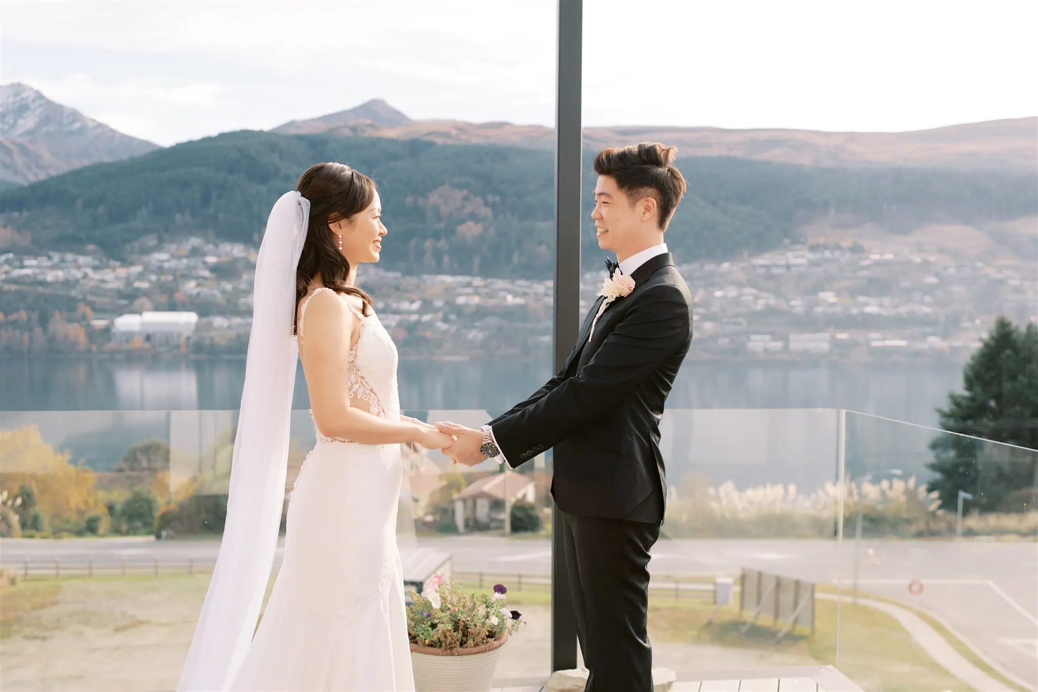 queenstown new zealand heli wedding elopement photographer videographer | A bride and groom hold hands, facing each other outdoors in a stunning Queenstown setting, with mountains and a lake in the background. Perfect for capturing the essence of an intimate elopement with exceptional wedding photography.