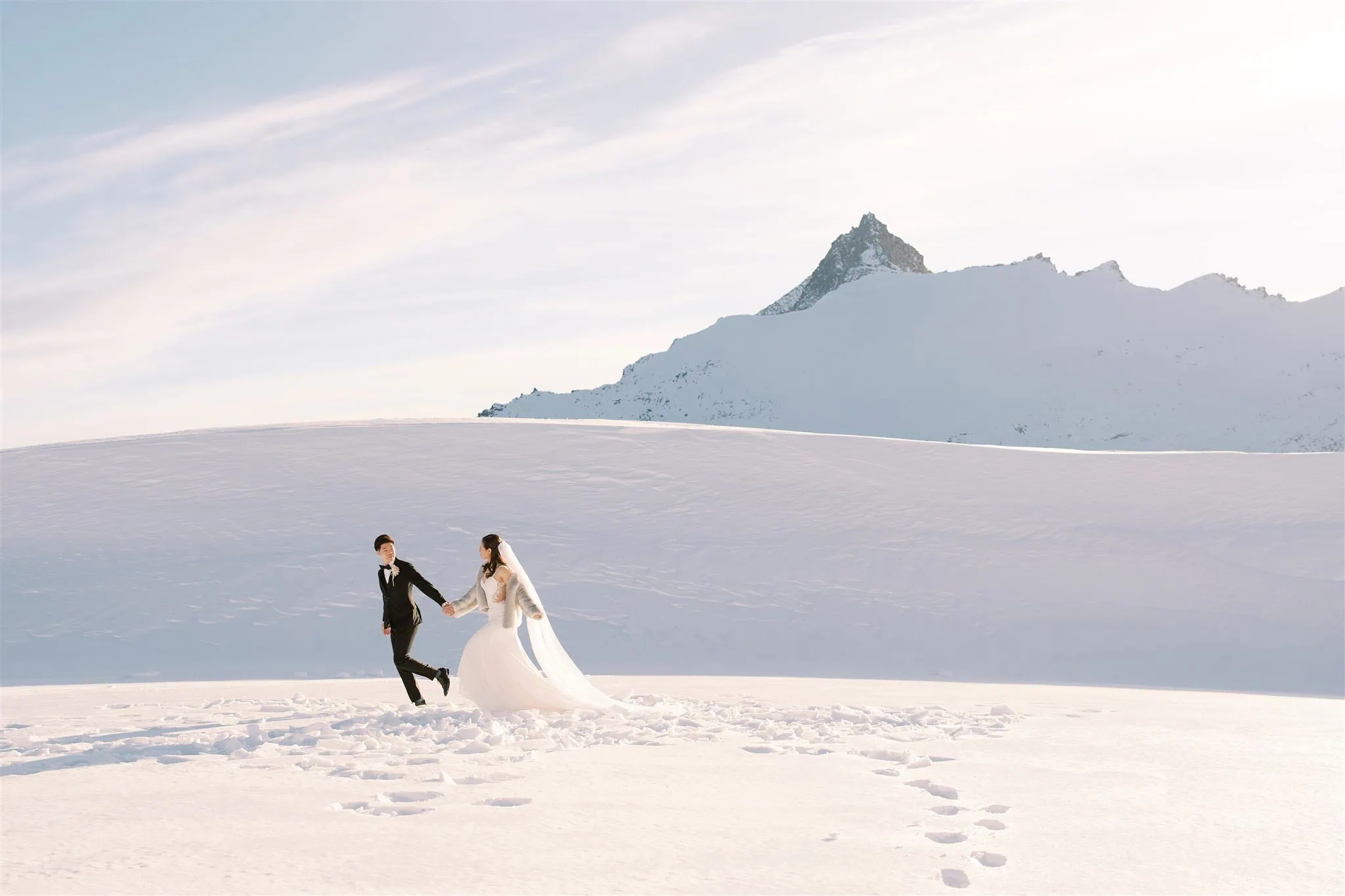 queenstown new zealand heli wedding elopement photographer videographer | Tiffany and Malcolm hold hands, surrounded by the enchanting snowy landscape of a Queenstown elopement, with majestic mountains as a backdrop.